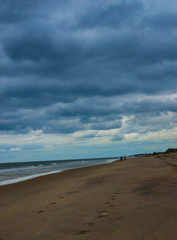 Couple walking along the ocean shore against a dramatic sky