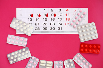 Calendar with paper blood drops and white, pink and red pills for female pain on bright pink background. Marking of the days of the menstrual cycle.