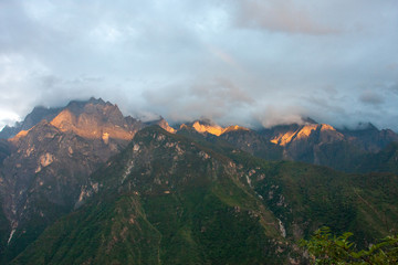 View from a guesthouse in the mountains of Yunnan during sunset with the top of the mountains being bathed in sunlight and the forests lying in the dark