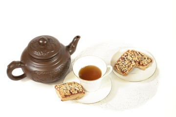 White Cup on saucer with tea and biscuits. Brown ceramic teapot for brewing tea. The cookies are in the saucer. Selective focus. On white background