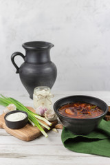 red borsch, a traditional national dish of Ukrainian cuisine. on the stock photo, is served in black pottery with sour cream, green onions and garlic on a light wooden background using green textile