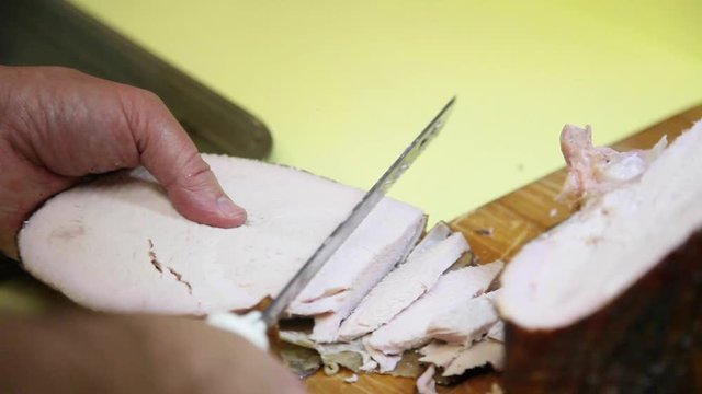 Close up of an electric carving knife slicing the breast of a smoked Thanksgiving turkey into serving size pieces. A slice is cut from the breast and sliced into smaller pieces. The skin easily peels.