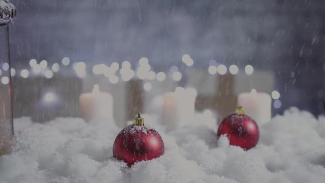snow falls on christmas balls and candles