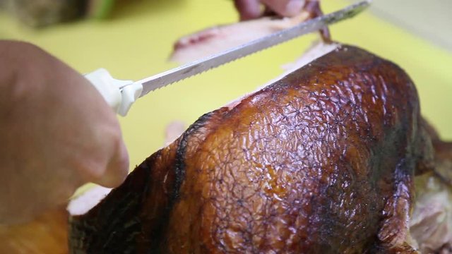Closeup of the serrated edges of the blades of an electric carving knife as it slices through a smoked Thanksgiving turkey. The skin is crisp and textured and the meat pulls easily away from the flesh