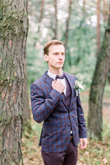 Handsome elegant groom in checkered dark violet suit is standing in the forest. Stylish wedding grooms photo. Rustic portrait.