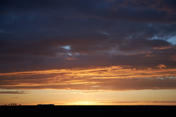 Orange rays of the sun at sunset illuminate dense clouds