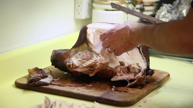 Hands of a man carve a smoked turkey for a Thanksgiving dinner. He easily pulls the dark meat off and slices the breast with a electric carving knife. The meat falls off the bone and is juicy.
