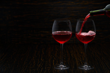 Pouring red wine into the glasses against wooden background