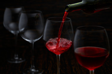 Red wine pouring into glasses from bottle, selective focus