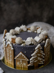 Obraz na płótnie Canvas Christmas gray cake decoraited of gingerbread cookies in shape of homes and snowy christmas trees, marshmallows, snowflakes, sweets. Christmas, New Year greeting card. Gray background. Copy space.