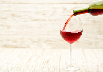 Pour red wine into a glass on white wooden background, selective focus.