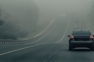 Fototapeta Cars in fog driving on a highway in dangerous weather. Bad winter weather and automobile traffic on the road. Vehicles with fog lights in a haze on a forest freeway in the morning. Low visibility obraz