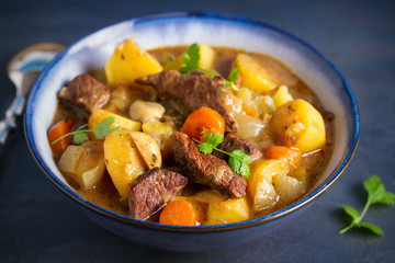Beef meat stewed with potatoes, carrots and spices in bowl on dark gray background.  horizontal...