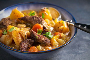 Beef meat stewed with potatoes, carrots and spices in bowl on dark gray background.  horizontal image
