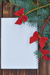 White sheet of paper and spruce branches with bows on a wooden background.