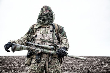 Army sniper standing in field with rifle