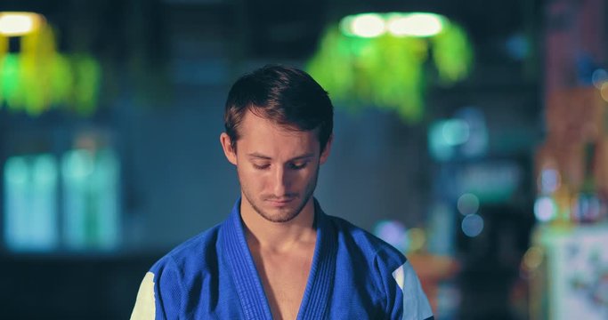 Cute fighter in a blue kimono prepares for battle, looks up, looks at the enemy. Young male judoka is attuned to the fight. Portrait view.