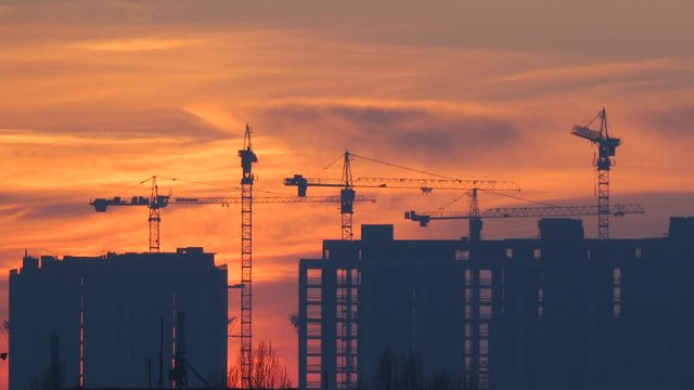 Construction of a high-rise building on a sunset background. Construction site with the silhouettes of cranes and apartments. Urbanization. The development of megacities. City landscape