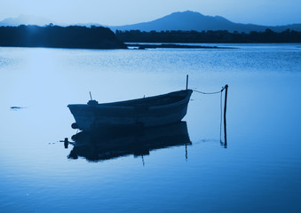 Fishing boat in the lake at the sunset in blue monochrome color tone