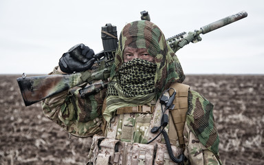 Army sniper standing in field with rifle
