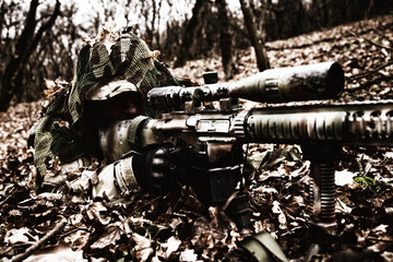 Army sniper hiding on ground in forest leaves