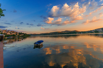A boat floating peacefully on a very still and quiet lake at dusk in Kastoria, Greece. Beautiful sunset colours of blue, pink, yellow and orange in the sky.