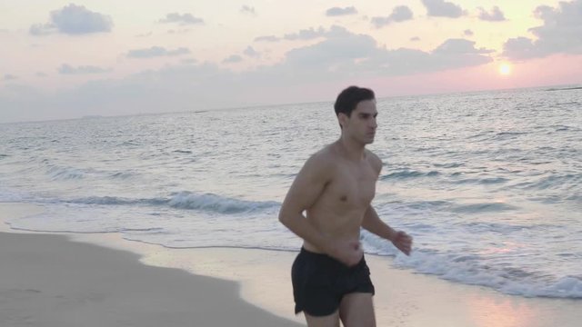 Athletic young runner jogging alone on beach in the evening