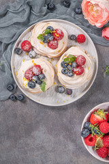 Mini pavlova meringue cakes with fresh raspberries and blueberries with mint leaves.