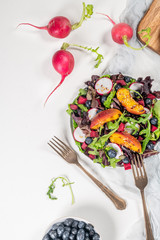 Fresh spring salad with rucola, lettuce, blueberries, radish, beet and slices of peach. White background with free text space. Top view