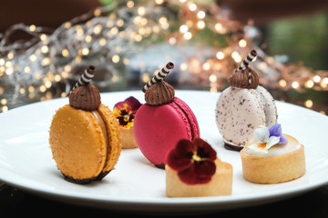 Close up of sweet colourful macarons on a white platy, Christmas lights in background