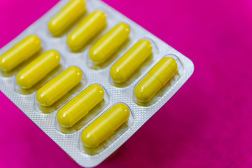 Yellow antibiotic capsules in a blister pack on a pink background. Medical pharmaceutical concept.