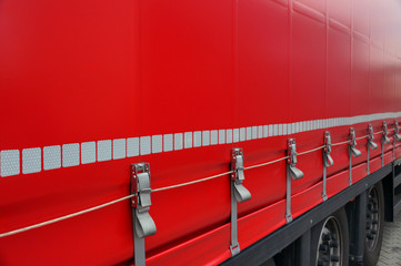 Red tarpaulin covering the semi-trailer of the trucks. Truck transport.