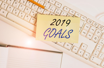 Word writing text 2019 Goals. Business photo showcasing something that you are trying to do or achieve for this year White pc keyboard with empty note paper and paper clips above white background