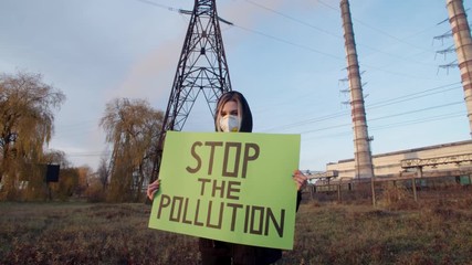 Woman Holding Poster With Stop Pollution Slogan outside near manufacturing business. Eco-Disaster. Green activism. Earth anti pollution action. Pullute production.Recycle industry system. Eco-business