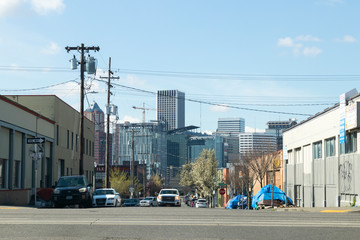 Homeless tents on the sidewalk next to a street and Portland Oregon city skyline seen in the...