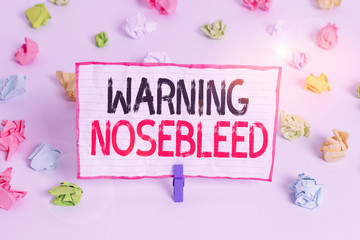 Handwriting text writing Warning Nosebleed. Conceptual photo caution on bleeding from the blood vessels in the nose Colored crumpled papers empty reminder white floor background clothespin