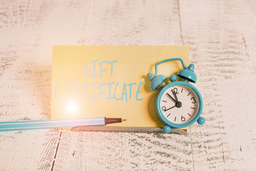 Handwriting text Gift Certificate. Conceptual photo certificate entitling the recipient to receive goods Mini blue alarm clock stand tilted above buffer wire in front of notepaper