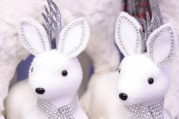 White fur deers Christmas home decoration in scarves from rhinestones and with silver horns. Winter festive background.
