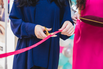 Process of cutting the red ribbon during the grand opening of the new shopping center mall building, opening of exhibition, close up view of red ribbon with people around