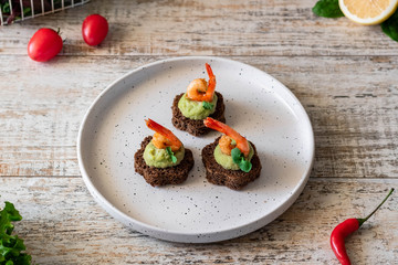 Canapes with avocado mousse and spicy shrimp on brown bread