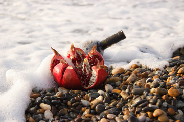 Ripe pomegranate fruit with bottle wine on the beach. Romantic day at the seaside.