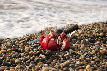 Ripe pomegranate fruit with bottle wine on the beach. Romantic day at the seaside.