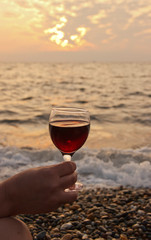 glass of red wine in his hand. Romantic day by the sea at sunset. The concept of wedding or Valentine Day celebrations.