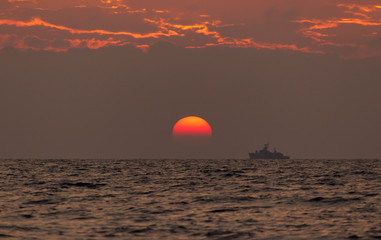 Sunset Beach Background. waves of the sea in the rays of the evening sunset. the sun goes below the horizon. On the horizon of the sea floats a ship