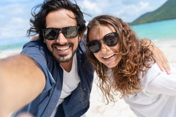Beach vacation couple taking selfie photograph using smartphone relaxing and having fun holding...