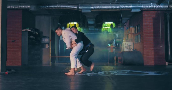 Male judoka grabs the opponent and applies a painful technique. Training judokas in the gym.