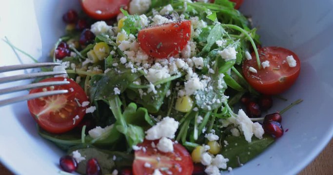 Fresh made arugula salad with cherry tomatoes, soft cheese, sweetcorn kernel and pomegranate seed on plate on rotating stand, close up