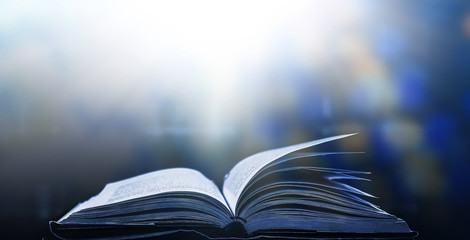 An ancient book that opens with magic, the magic light in the darkness on the wooden table, by the bright light shining down as the power to search for knowledge, religion and background