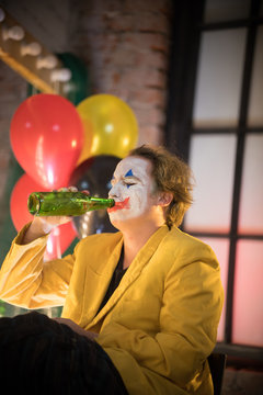 Clown concept - a sad tired man clown in yellow jacket drinking alcohol in the dressing room