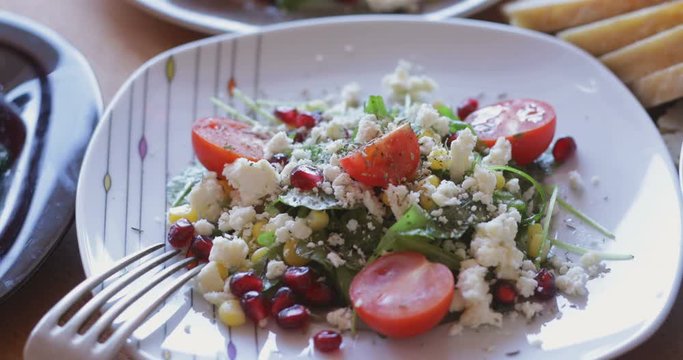 Fresh made arugula salad with cherry tomatoes, soft cheese, sweetcorn kernel and pomegranate seed on plate on rotating stand, close up